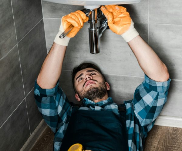 bearded repairman fixing water damage with adjustable wrench in bathroom